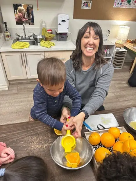 teacher helping preschooler juice an orange