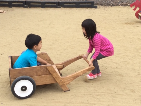 2 kids playing wood wheelbarrel