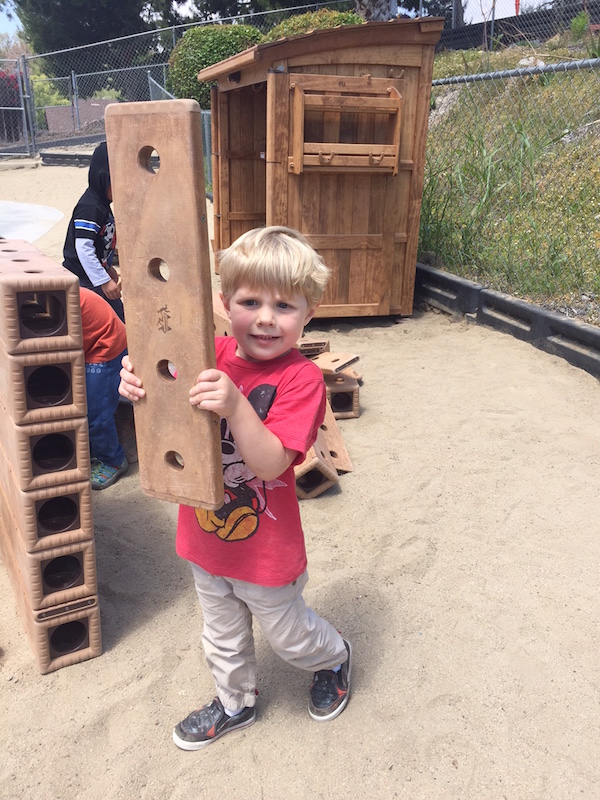 Preschool boy playing with large woodblock outdoor set