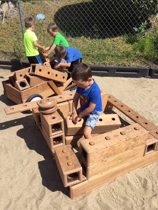 Preschool students with large wood building blocks on playground