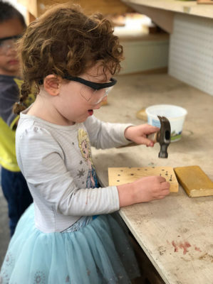 girl learning to use a hammer and nails