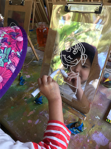 girl drawing faces on mirror at child care