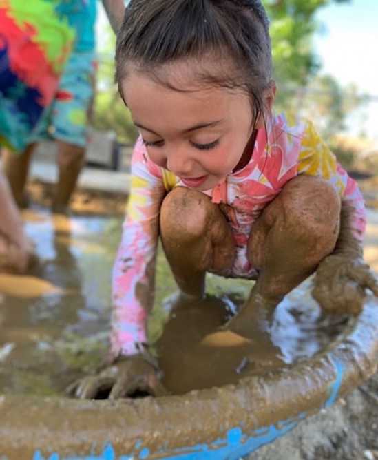 young girl in pink playing in mud